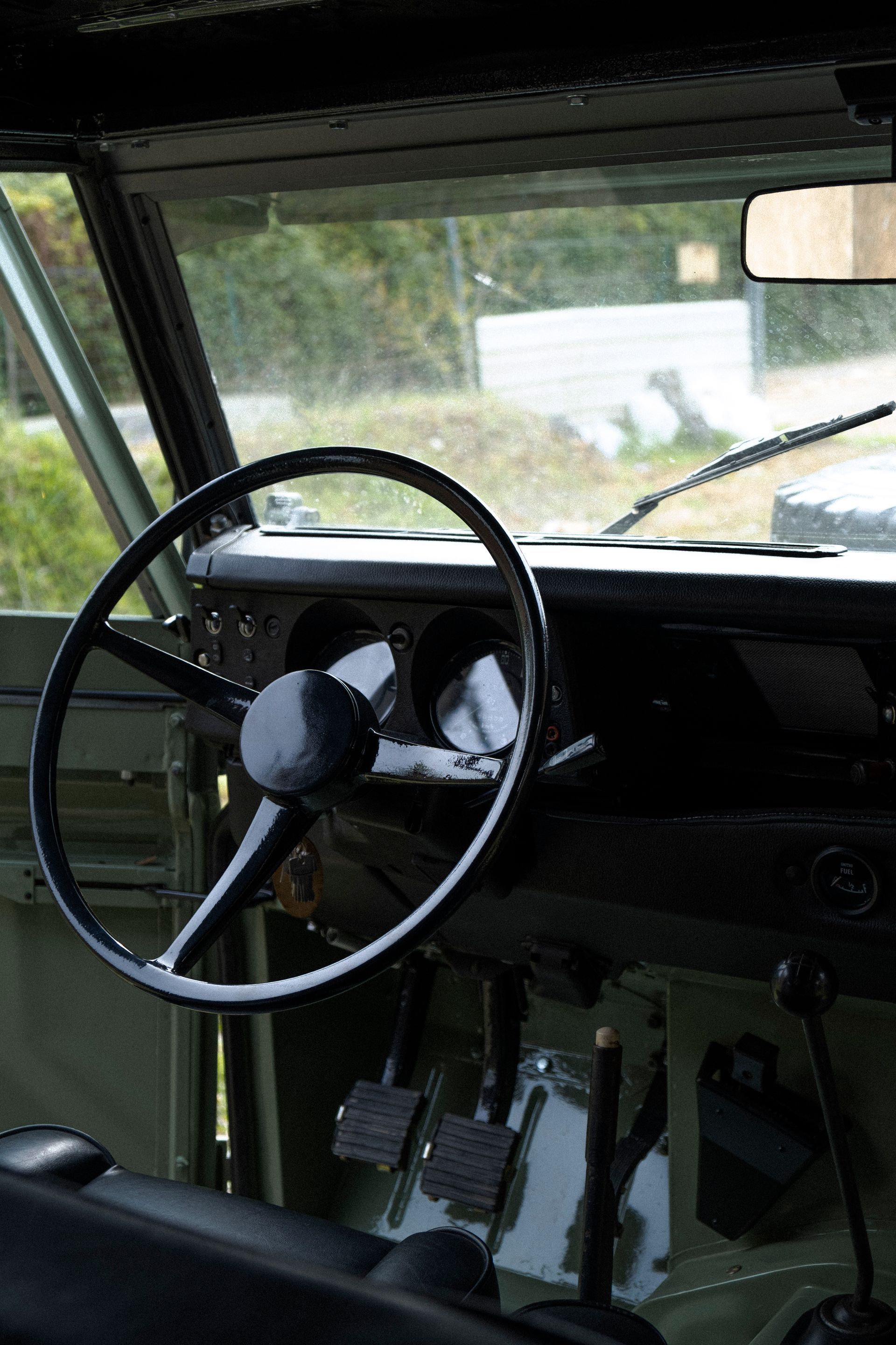 Intérieur d'un véhicule vert vintage : volant, jauges, pédales et vue du pare-brise.