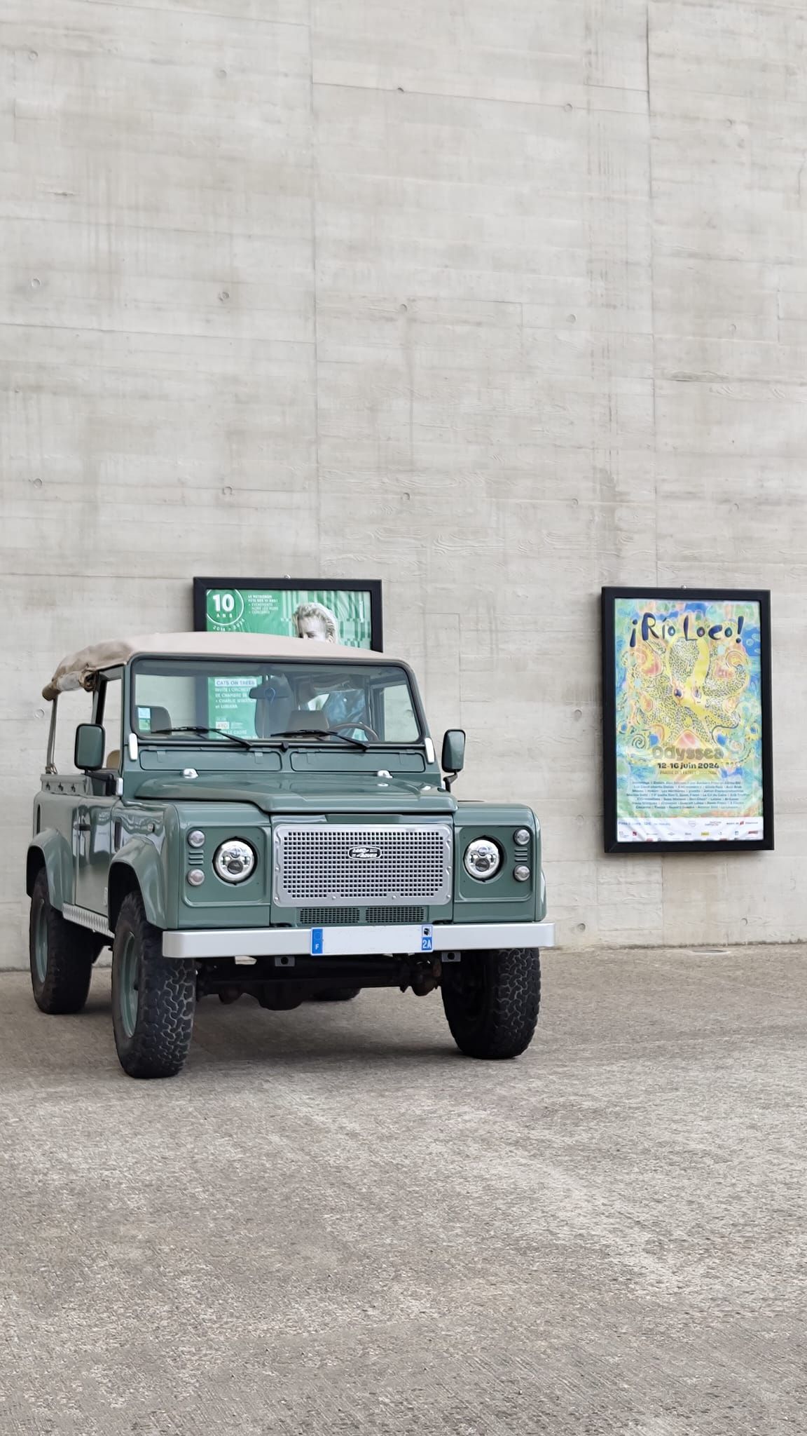 Land Rover Defender vert garé à côté d'un mur en béton avec des affiches encadrées.