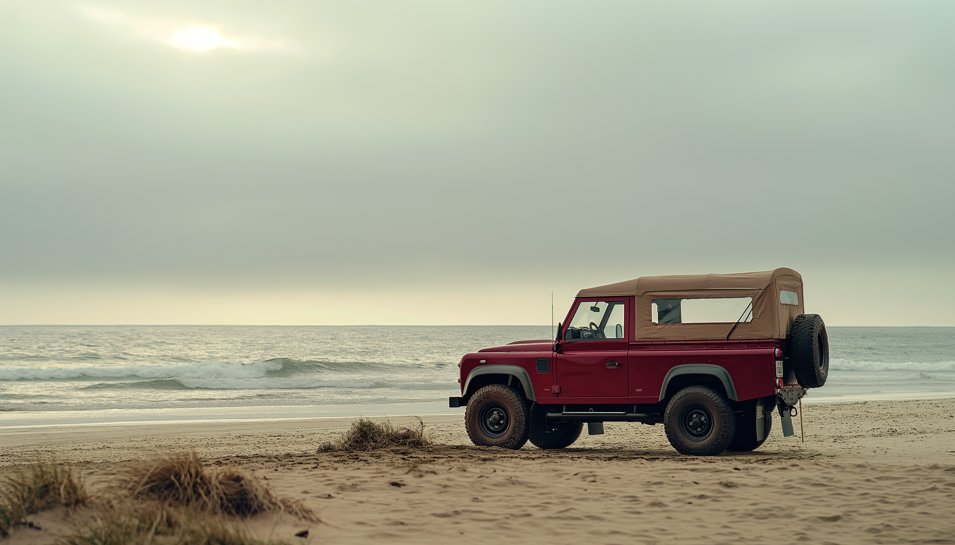 Véhicule tout-terrain décapotable rouge garé sur une plage de sable avec un ciel nuageux.