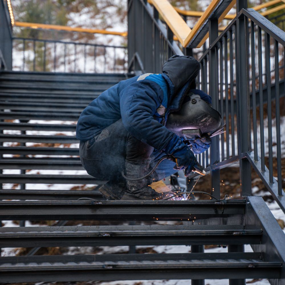 A man is welding a metal railing on a set of stairs.