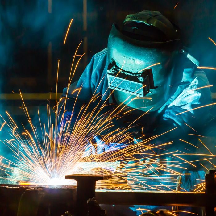 A man wearing a welding mask is welding a piece of metal.