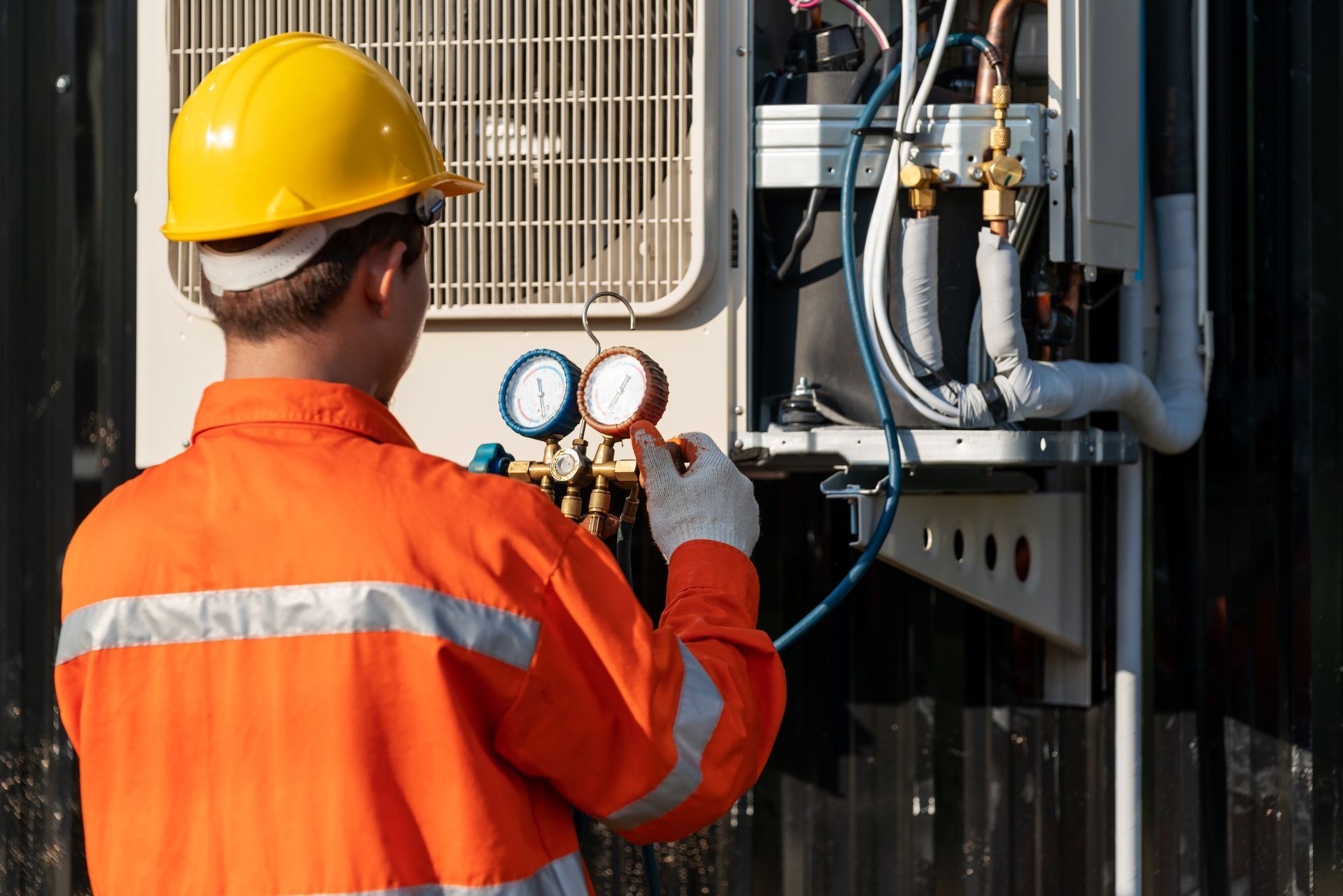 A technician, wearing safety gear, performs air conditioning repair, by using a tool.