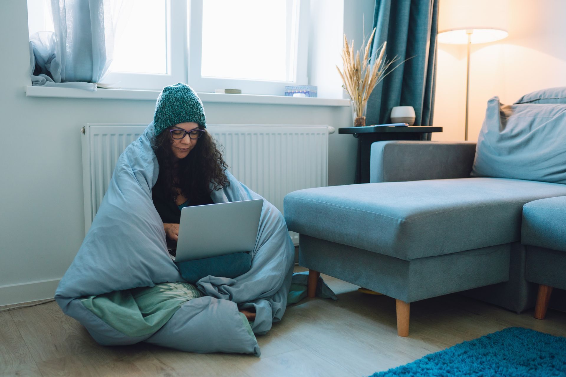 A woman wrapped in a blanket is sitting on the floor using a laptop computer.