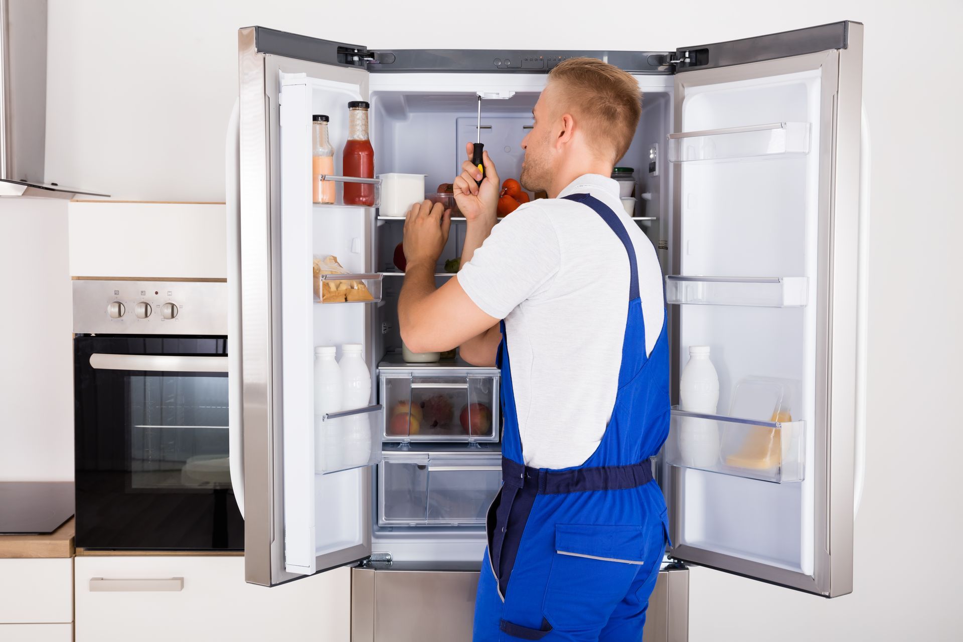 A technician is repairing a broken refrigerator appliance to restore its cooling functionality.