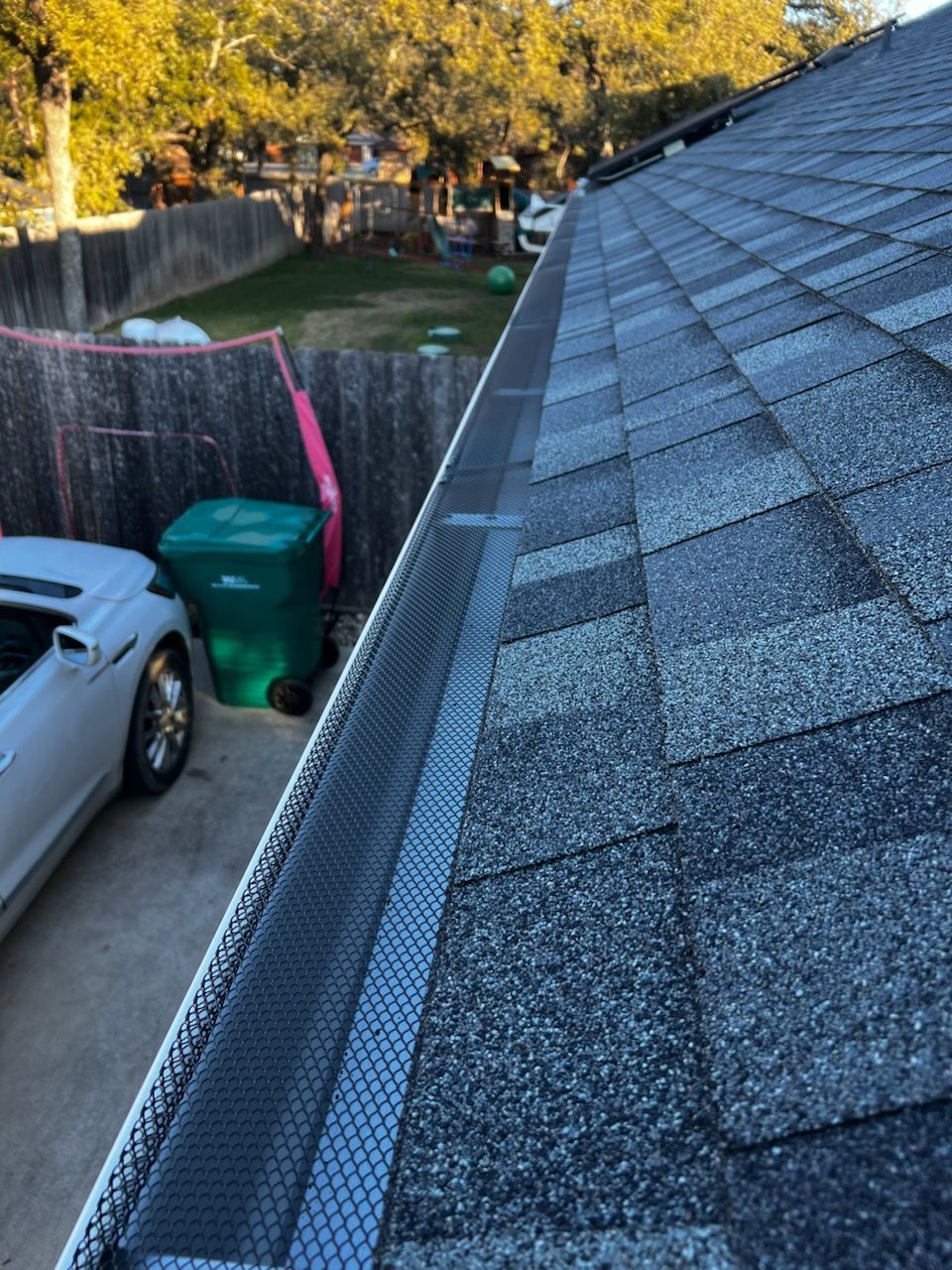 A car is parked in a driveway next to a gutter on a roof.