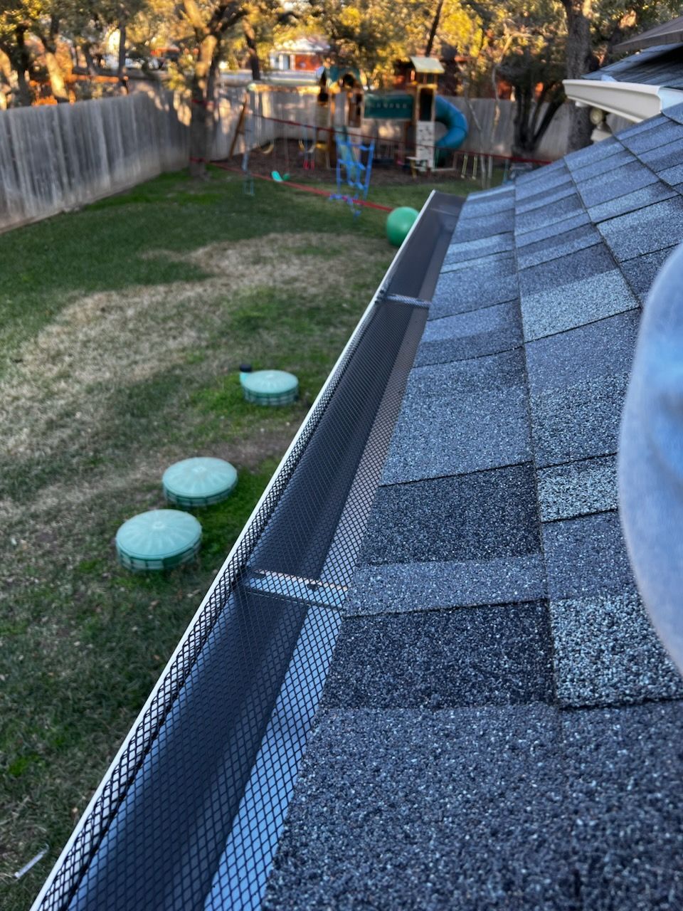 A person is standing on the roof of a house with a gutter.