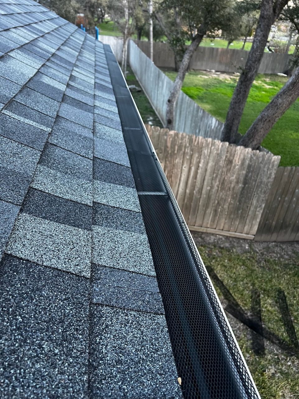 A gutter on the side of a roof next to a wooden fence.