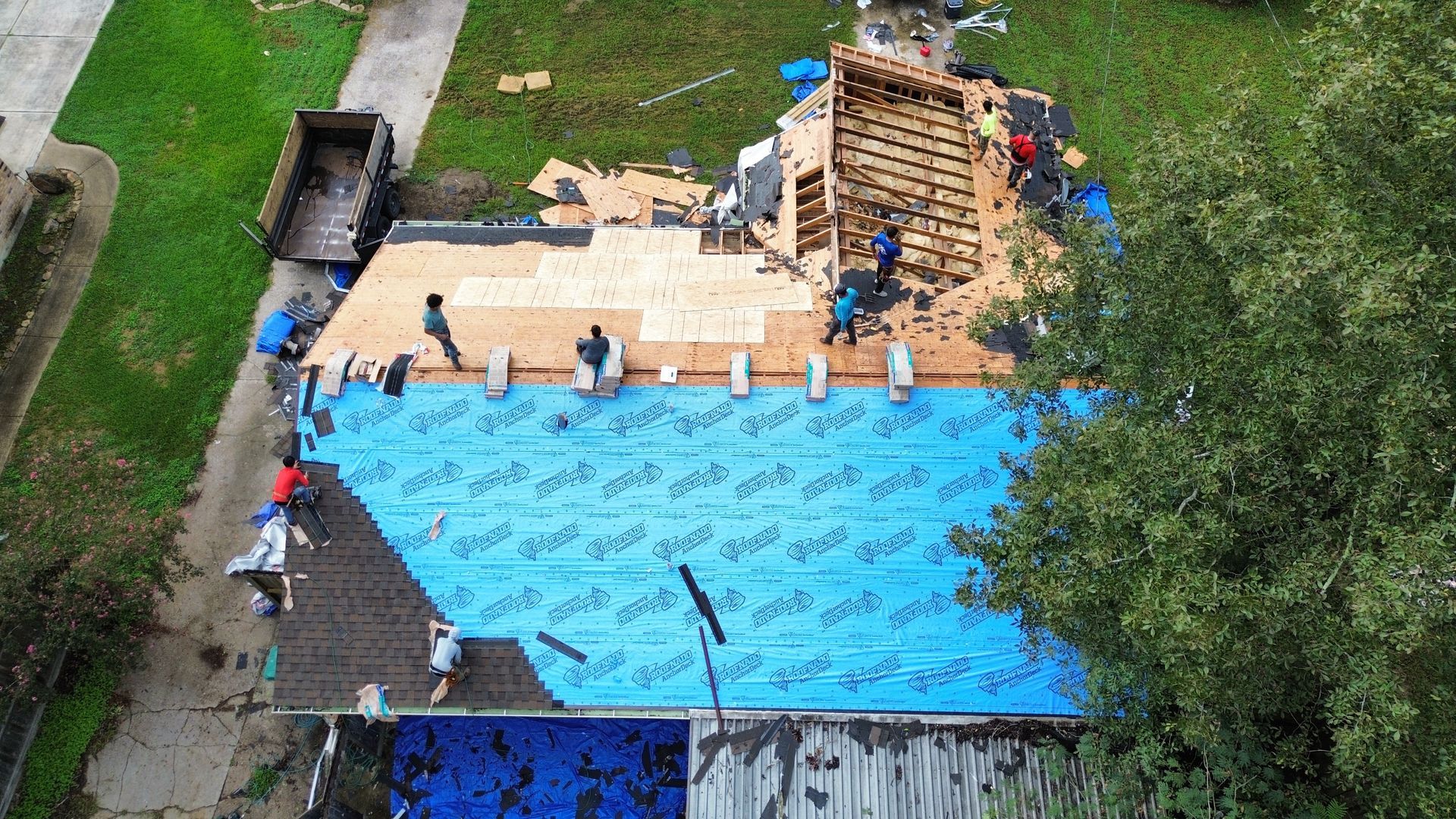An aerial view of a house under construction with a blue tarp on the roof.