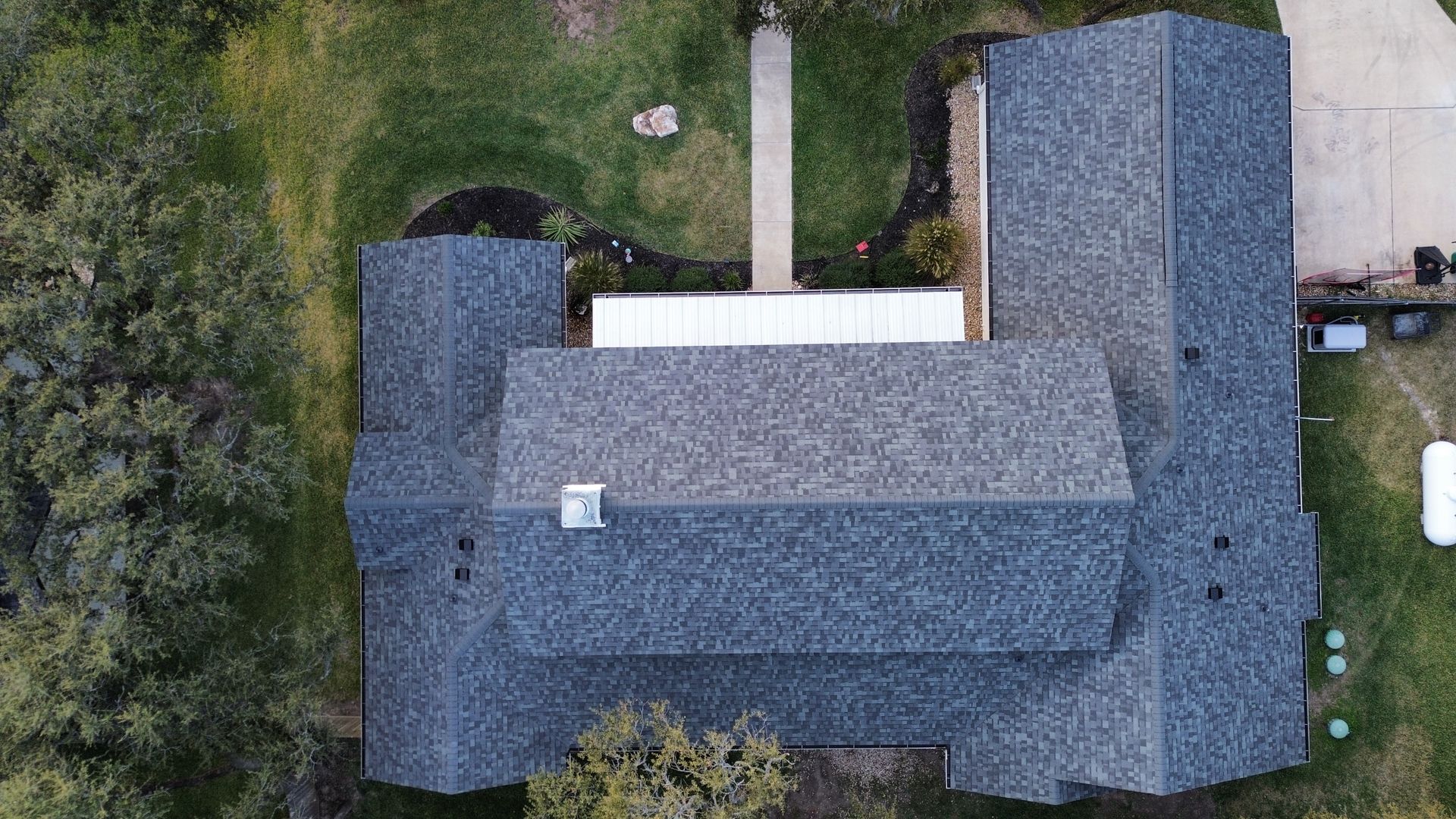 An aerial view of a house with a roof that is surrounded by trees.