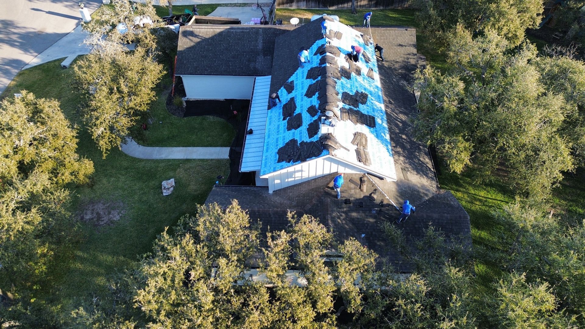 An aerial view of a house with a roof covered in blue tarps.