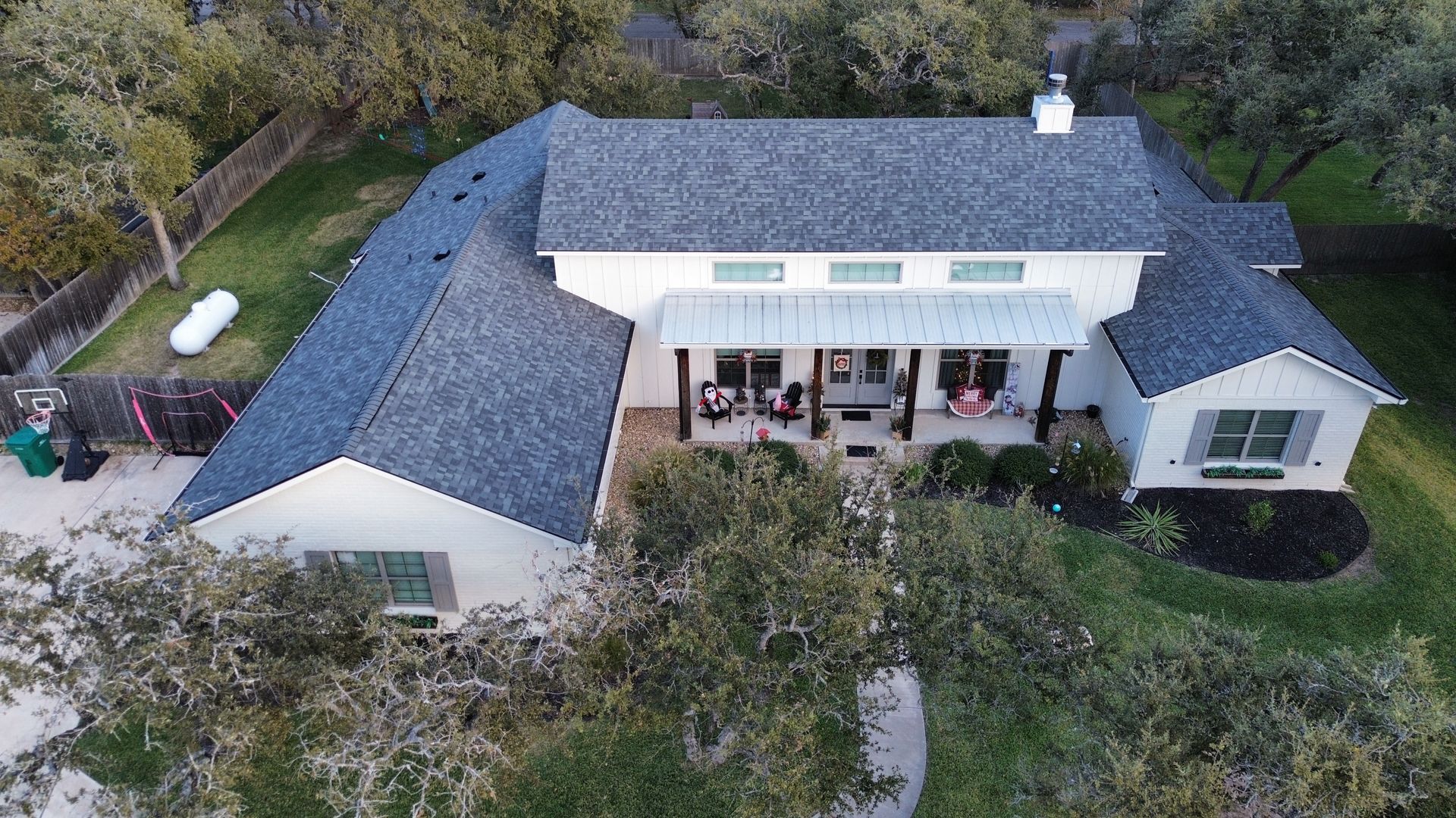 An aerial view of a large white house with a blue roof surrounded by trees.