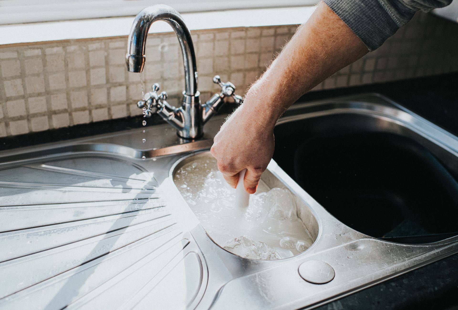 Hand plunging a water-filled kitchen sink to clear a clogged drain.