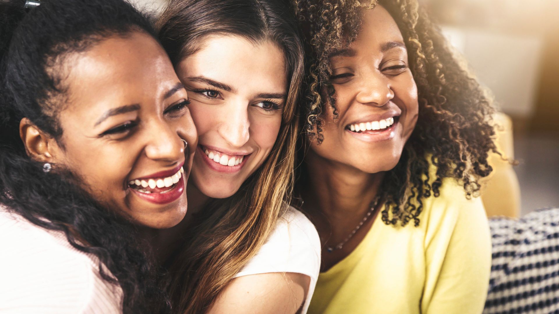 Three women smiling and laughing together, close-up.