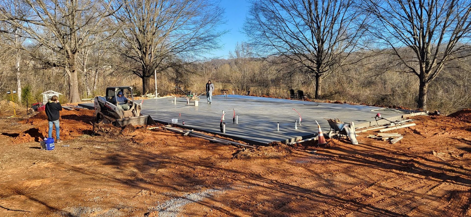 A concrete foundation for a house with a person standing next to it and trees in the background.