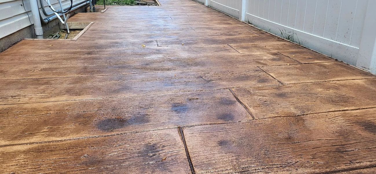 Brown textured concrete walkway with white fence and building.