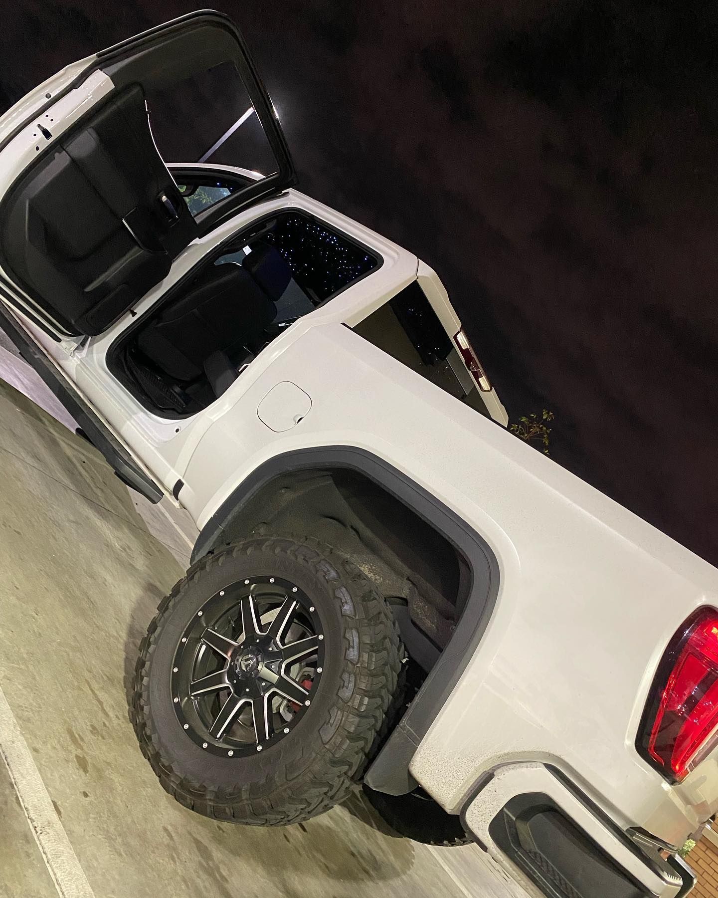 A white truck with the door open is parked in a parking lot at night.