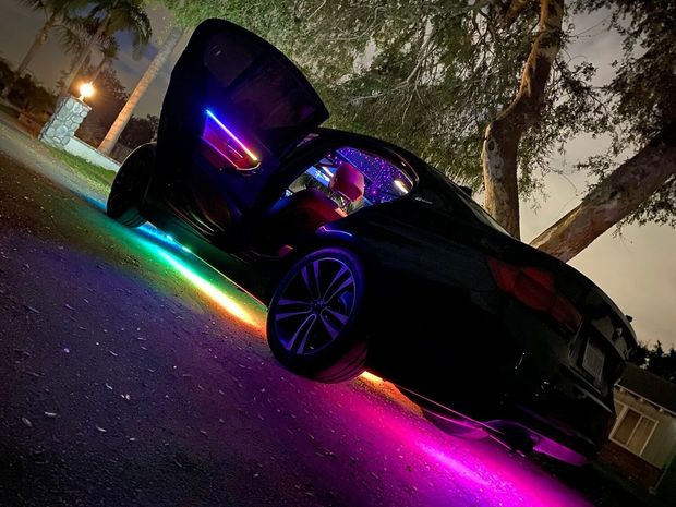 A black car with rainbow lights on it is parked on the side of the road.