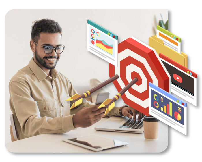 A man is sitting at a desk holding two arrows in front of a target.