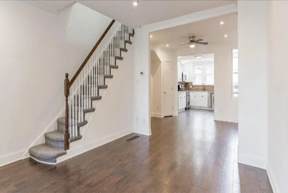 An empty living room with hardwood floors and stairs leading up to the second floor.