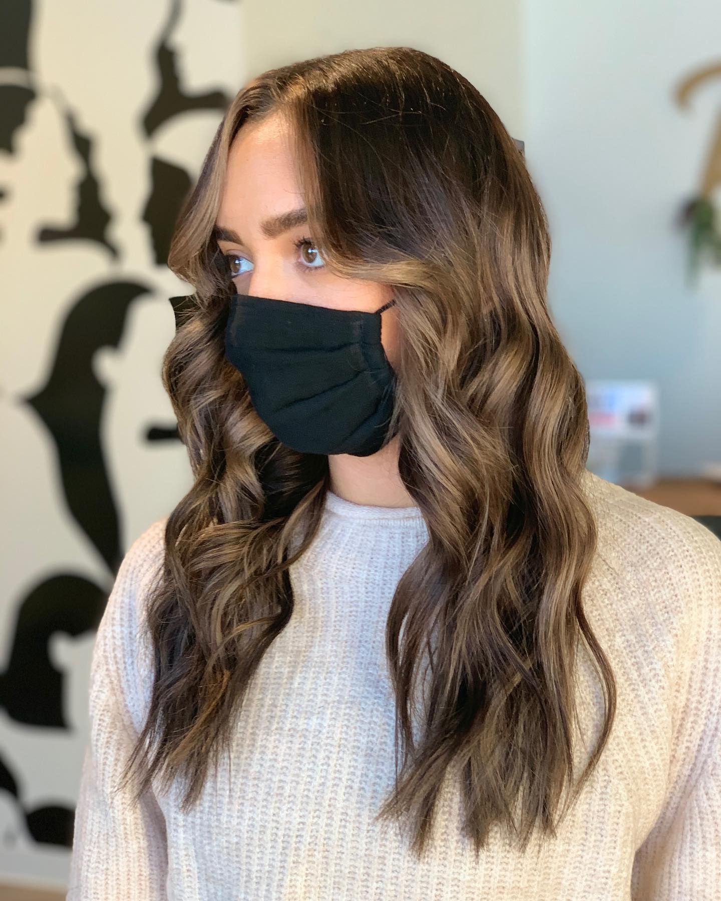 A woman wearing a black face mask and a sweater.