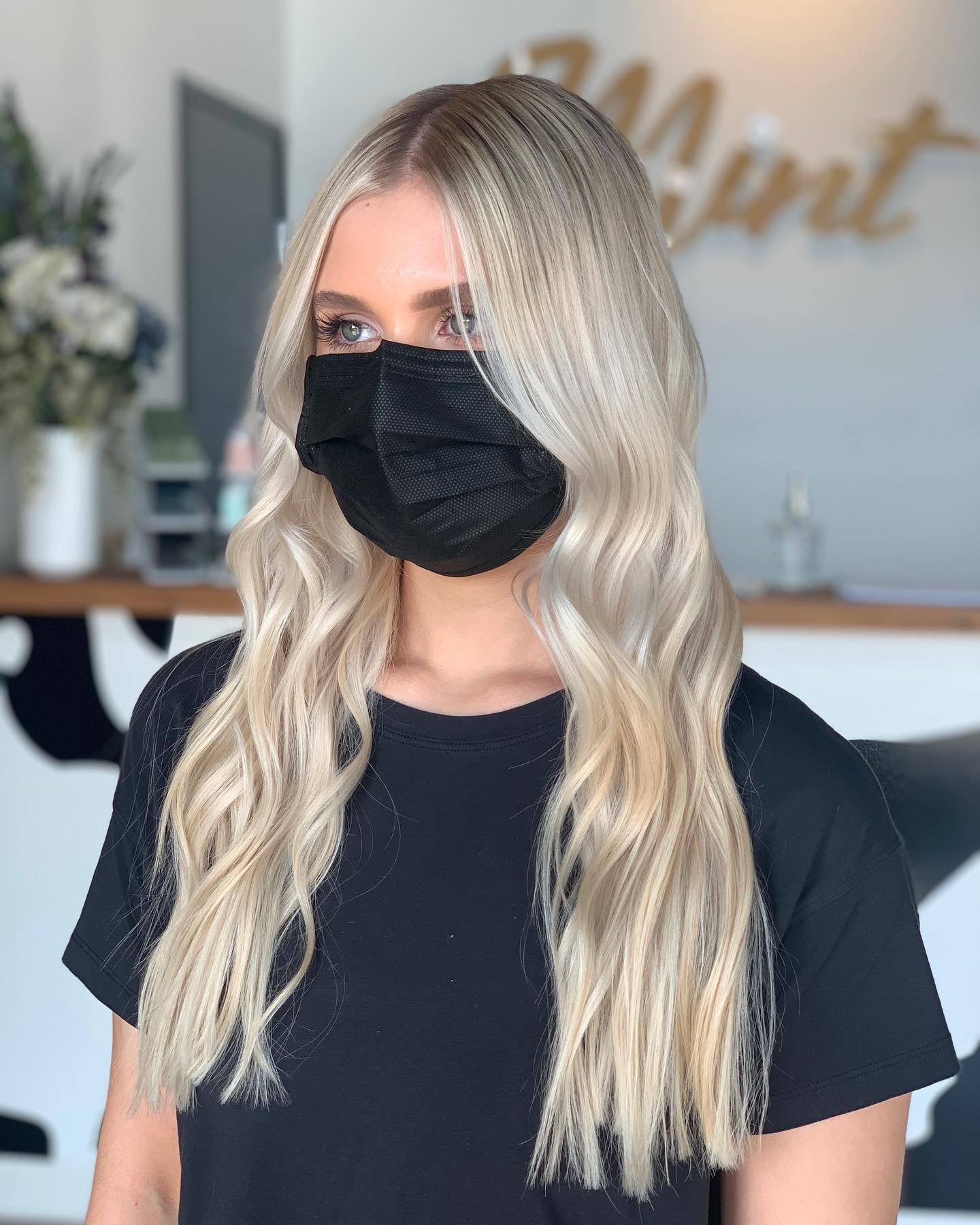 A woman with blonde hair is wearing a black face mask.