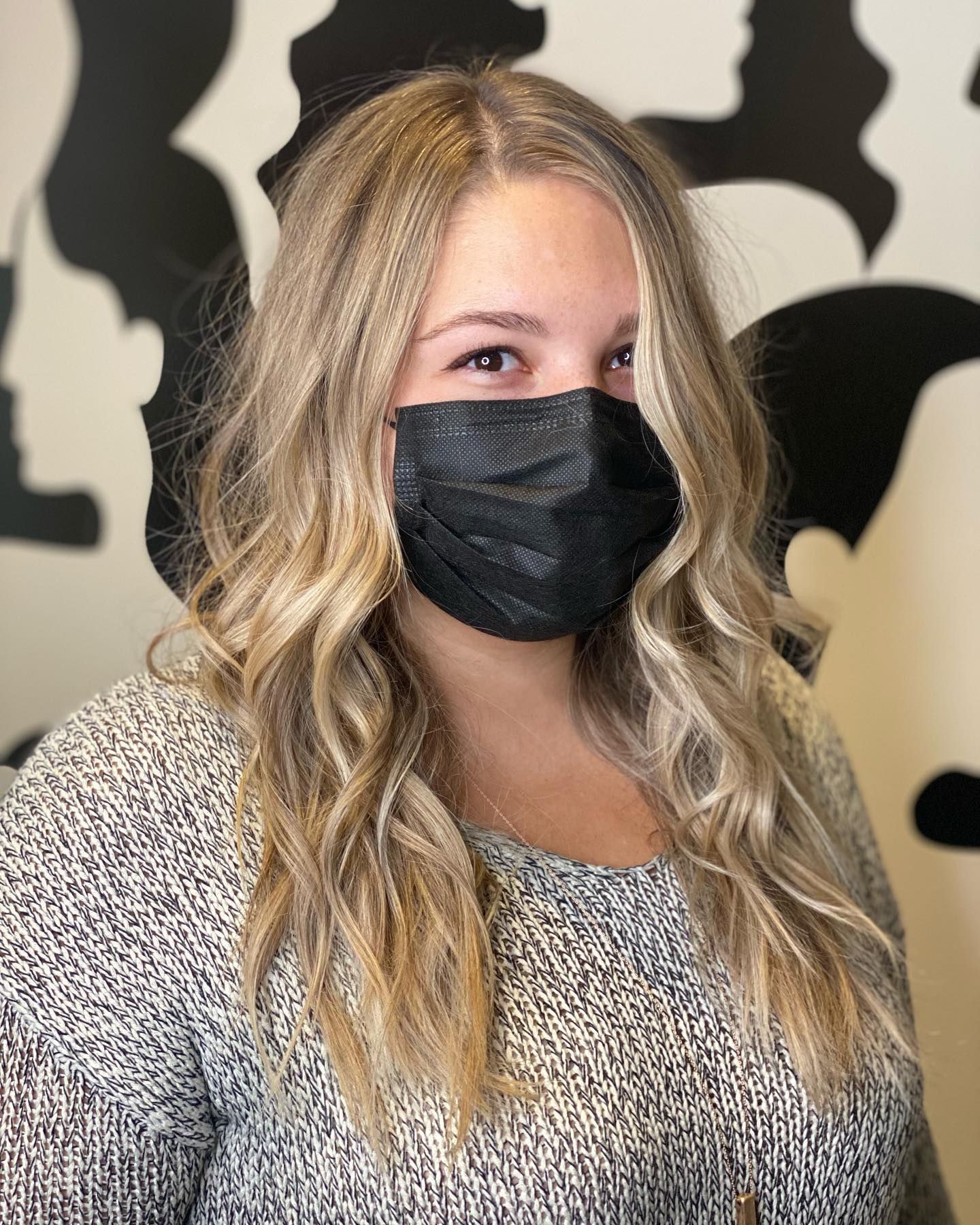 A woman with long blonde hair is wearing a black face mask.