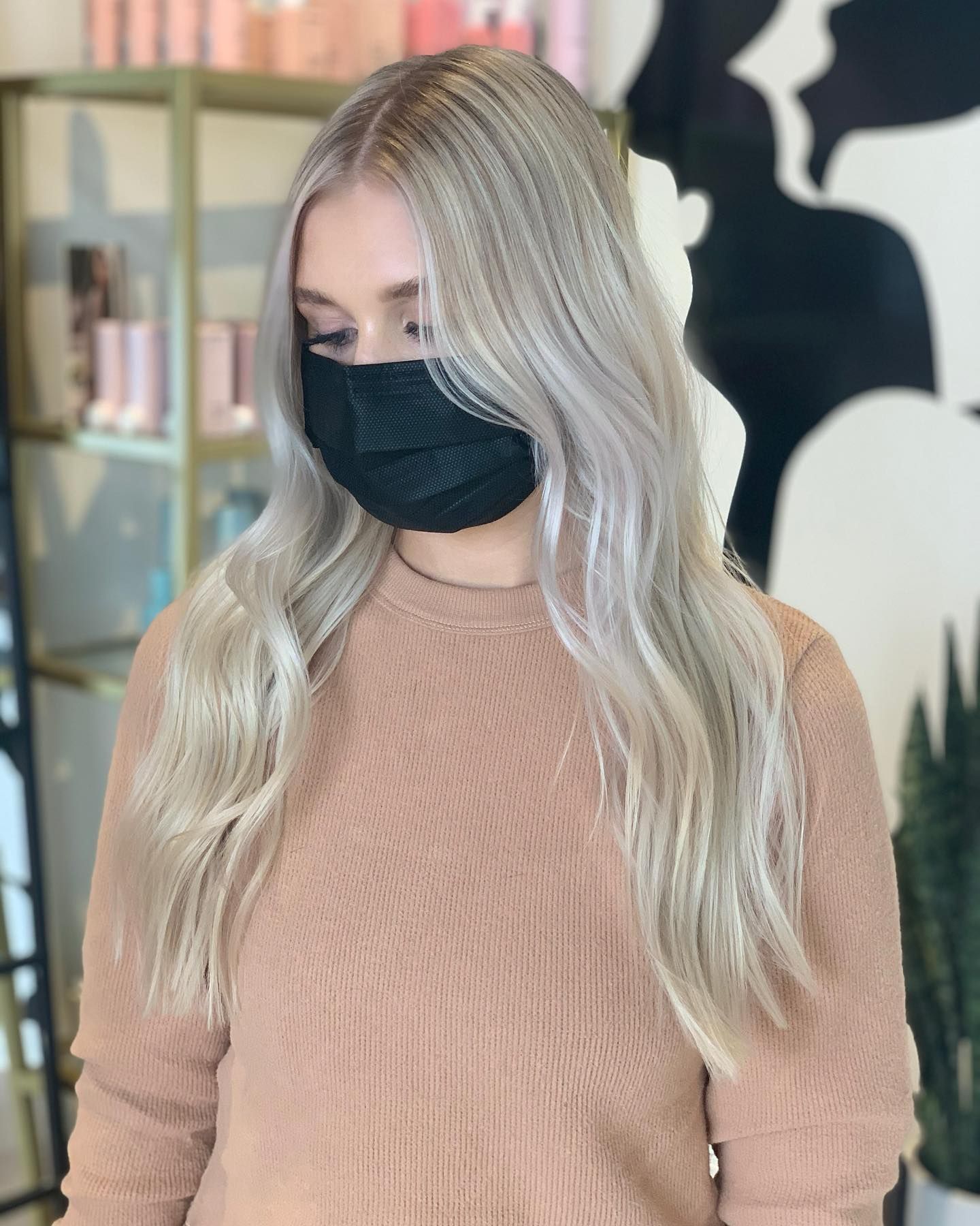 A woman wearing a mask and a brown sweater is standing in a room.