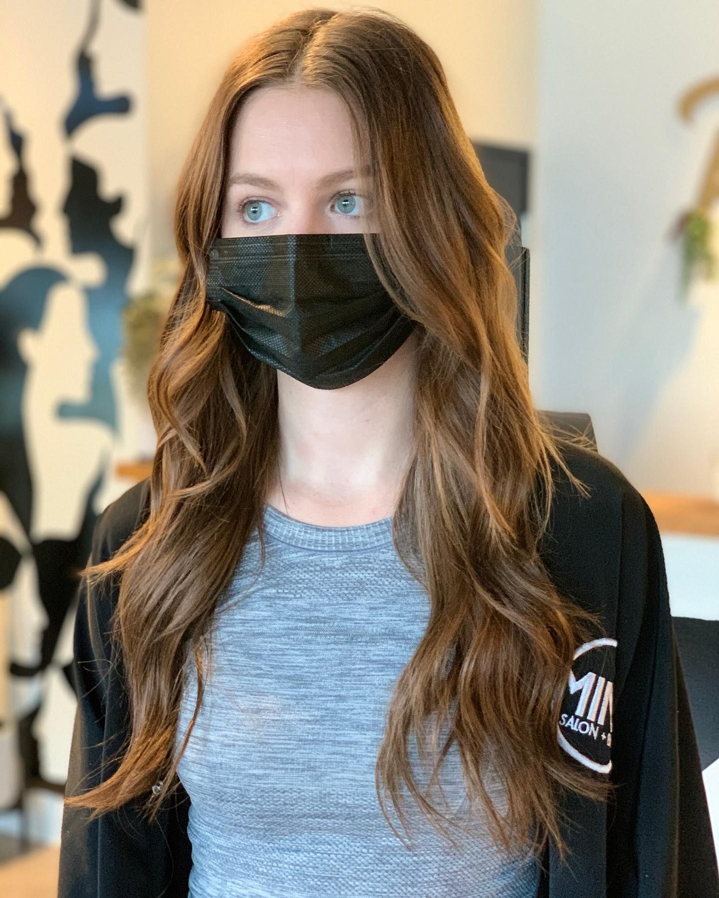 A woman with long hair is wearing a black face mask.