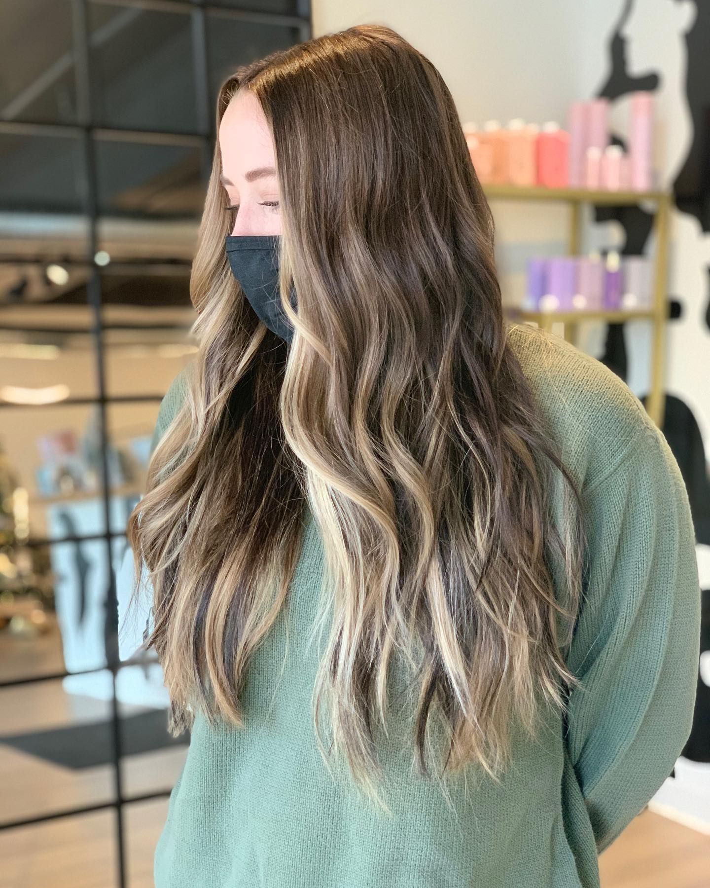 A woman wearing a mask and a green sweater is standing in a room.