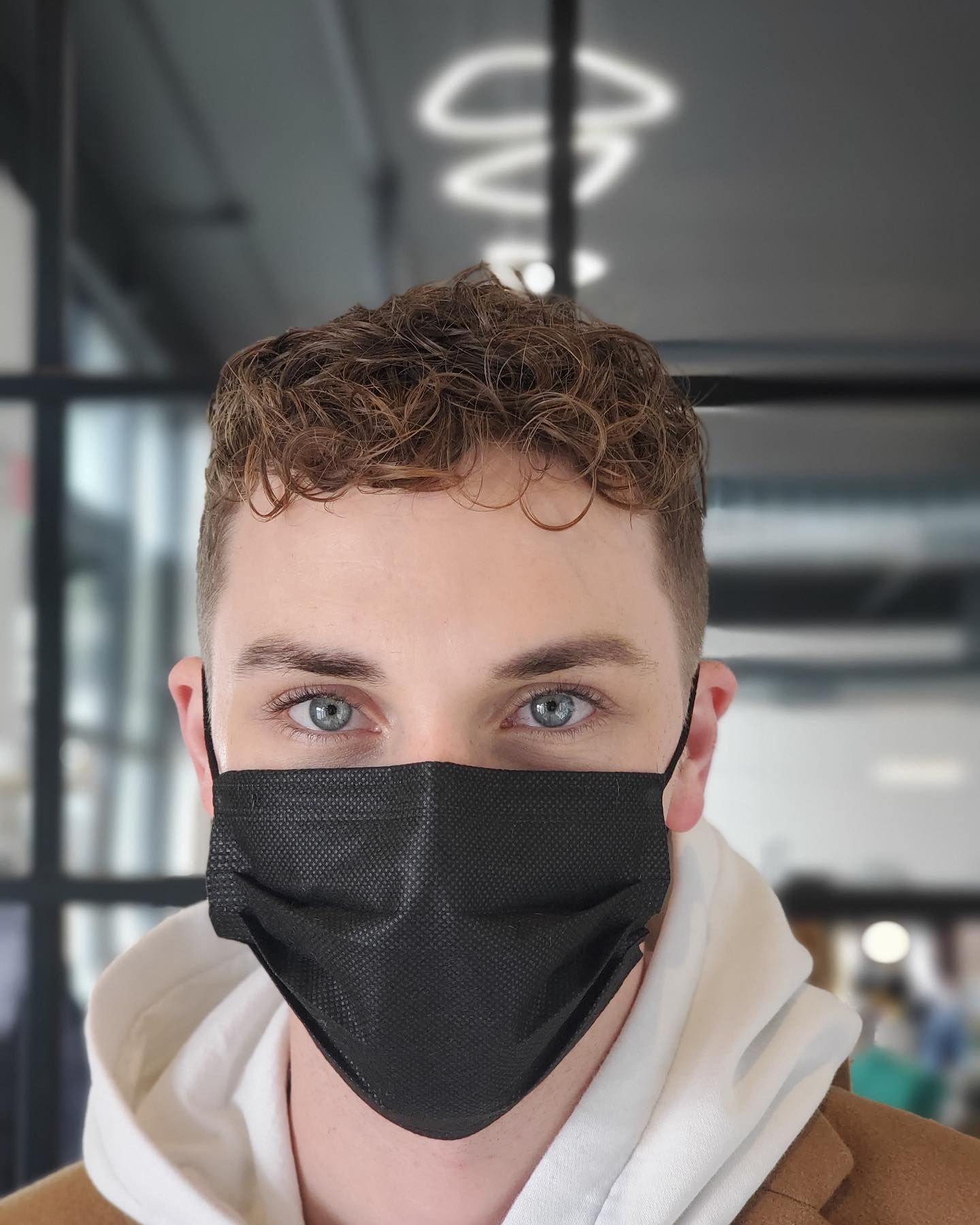 A man with curly hair wearing a black face mask