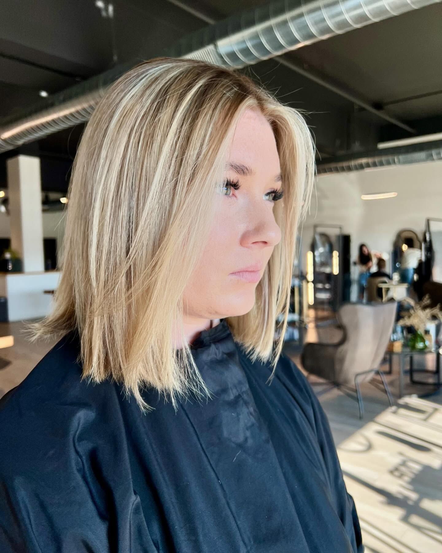 A woman with blonde hair is wearing a black jacket in a salon.