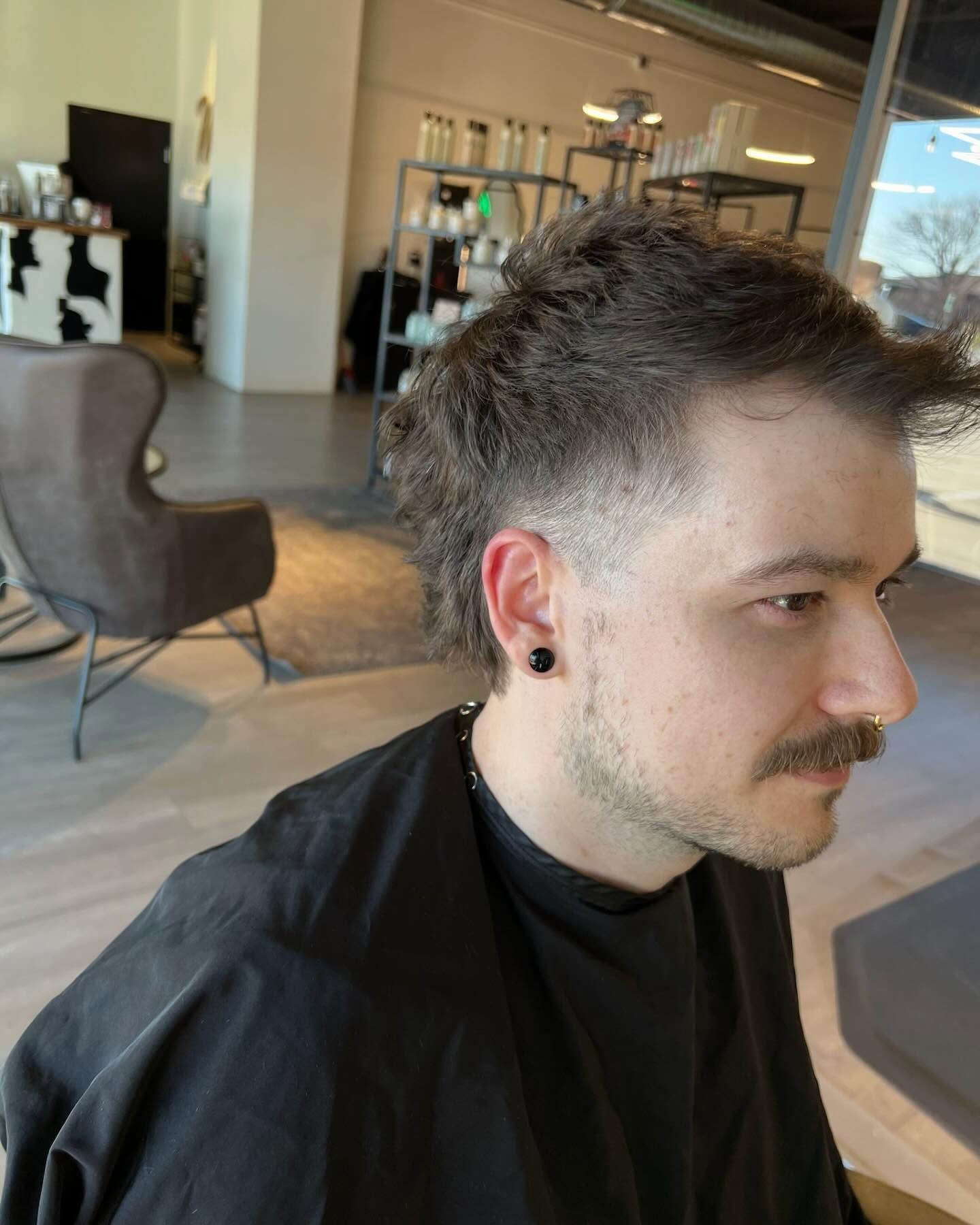 A man with a mustache is getting his hair cut in a salon.