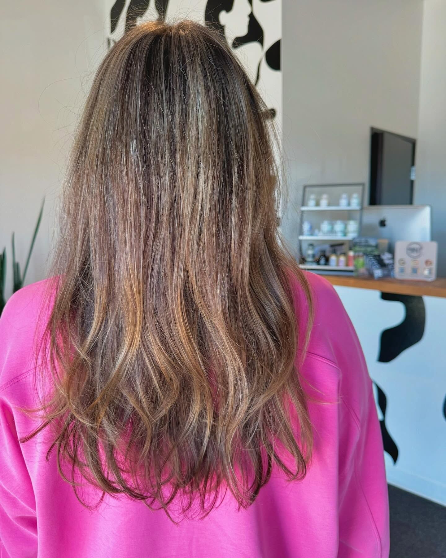 A woman with long hair is wearing a pink sweater and standing in a room.