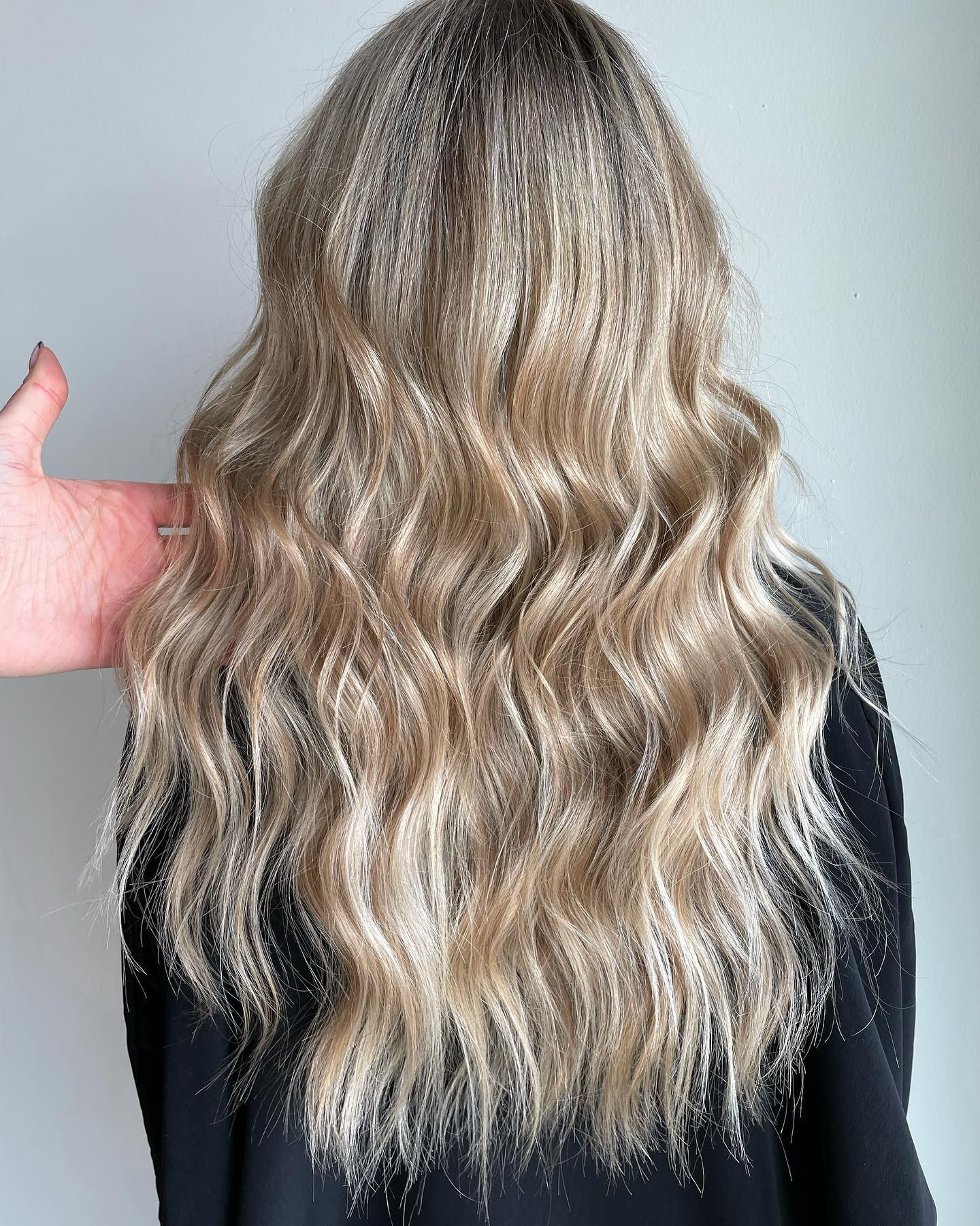 A woman with long blonde wavy hair is wearing a black shirt.