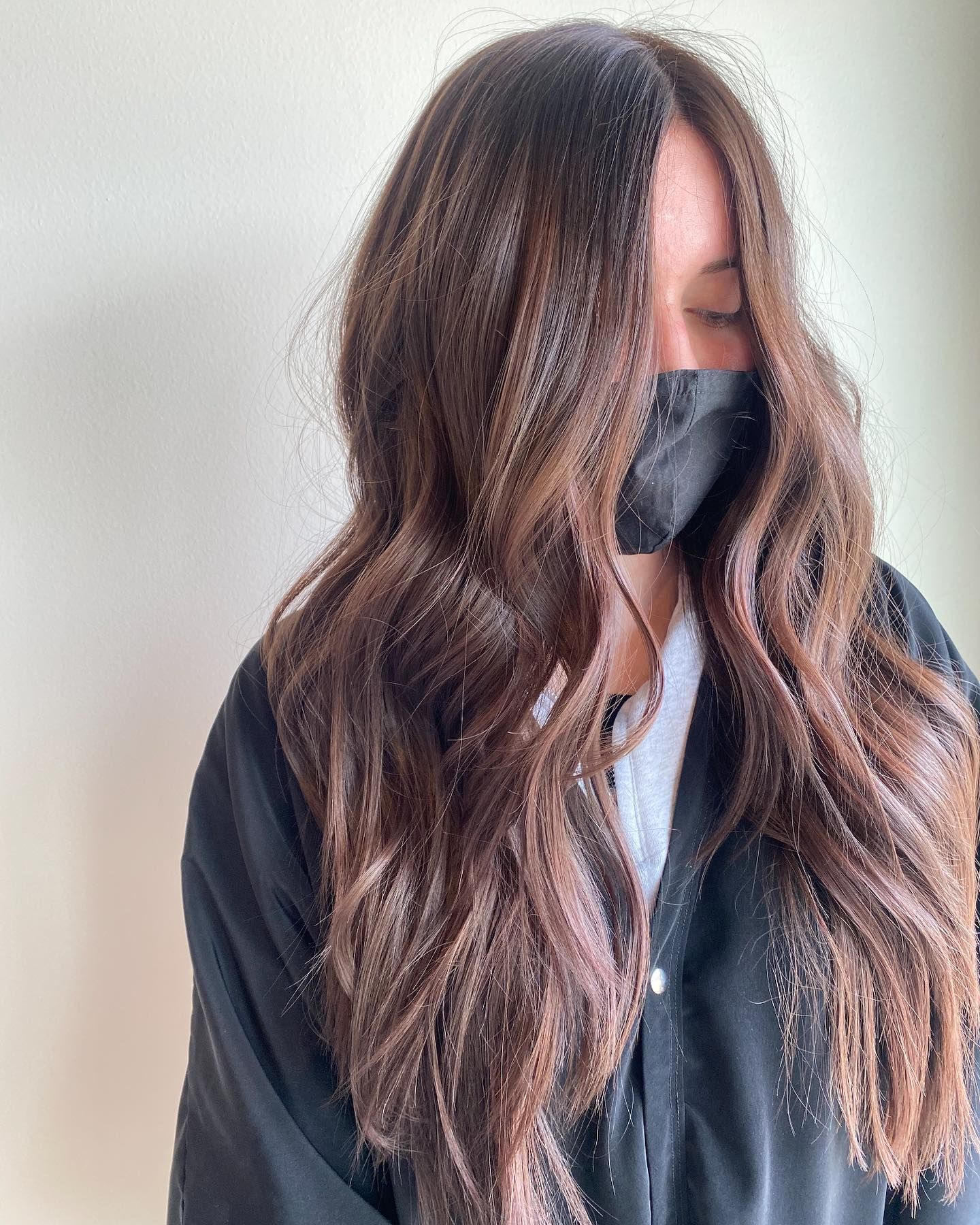 A woman with long brown hair is wearing a black mask.