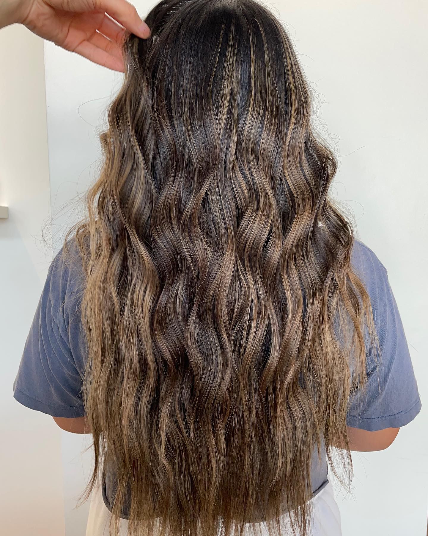A woman with long wavy hair is standing in front of a white wall.