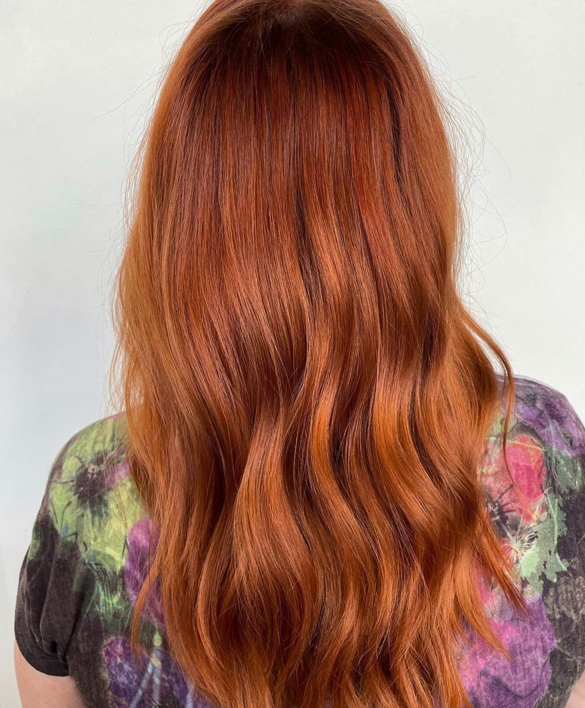A woman with long red hair is wearing a tie dye shirt.