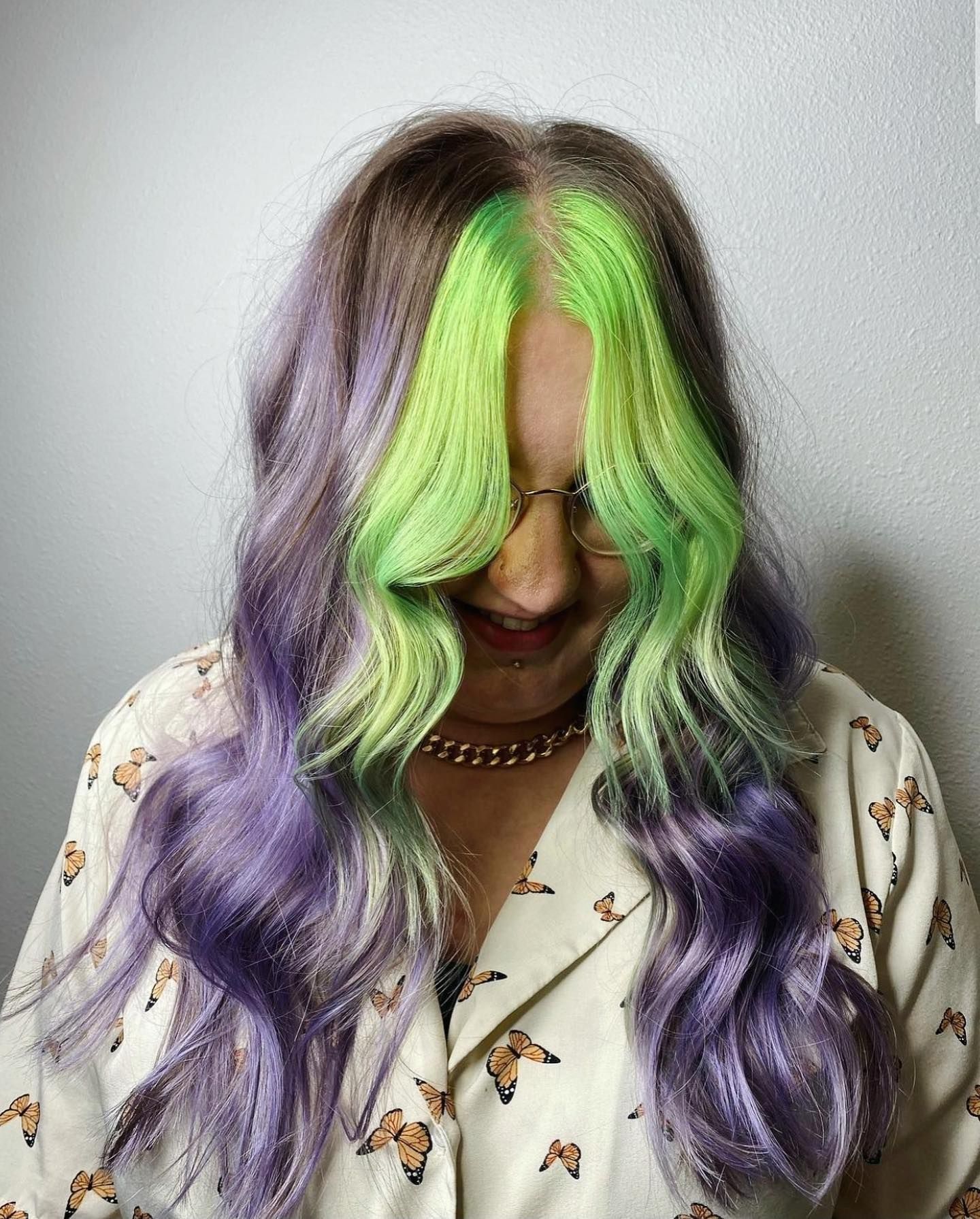 A woman with purple and green hair is smiling.