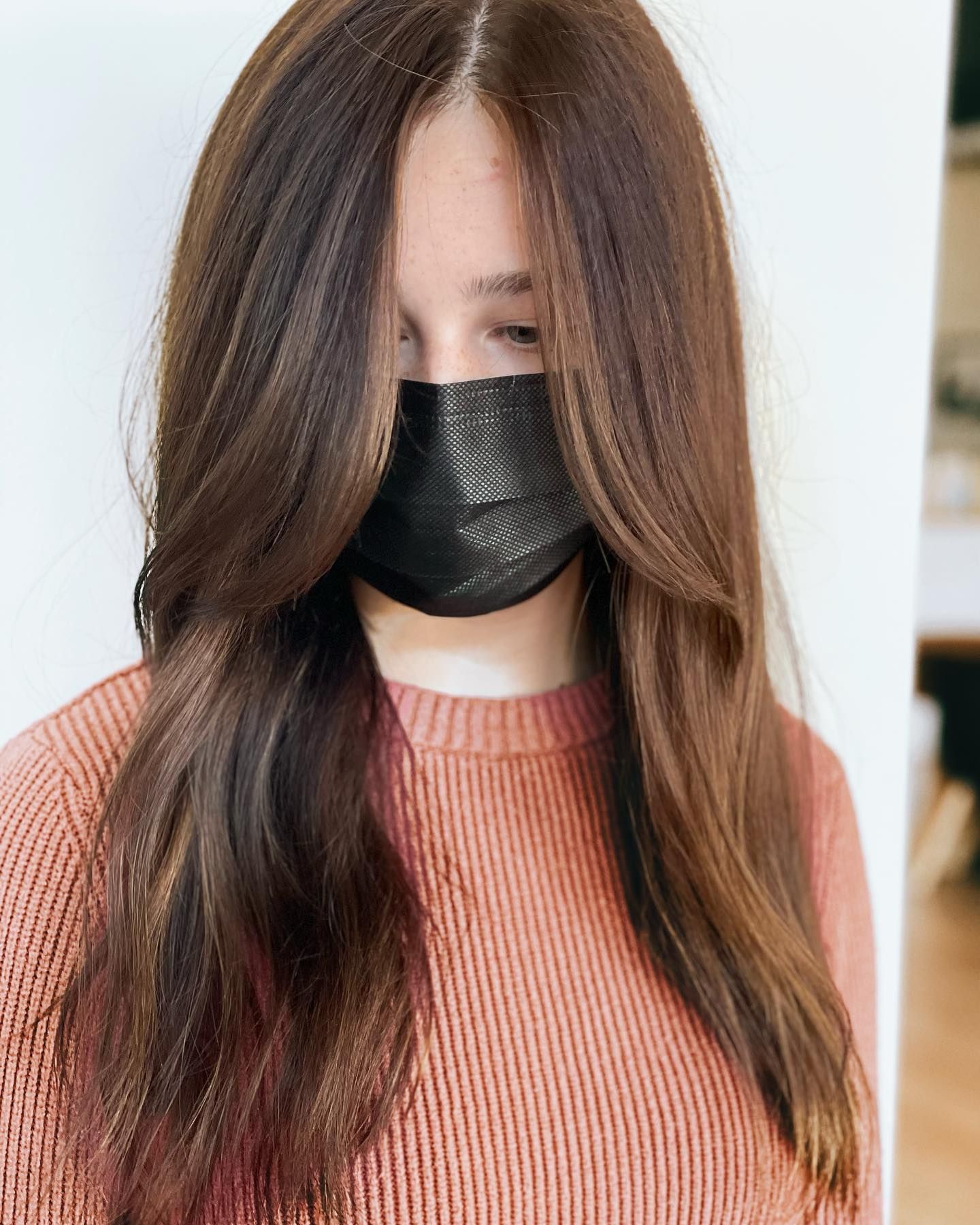 A woman wearing a mask and a pink sweater.