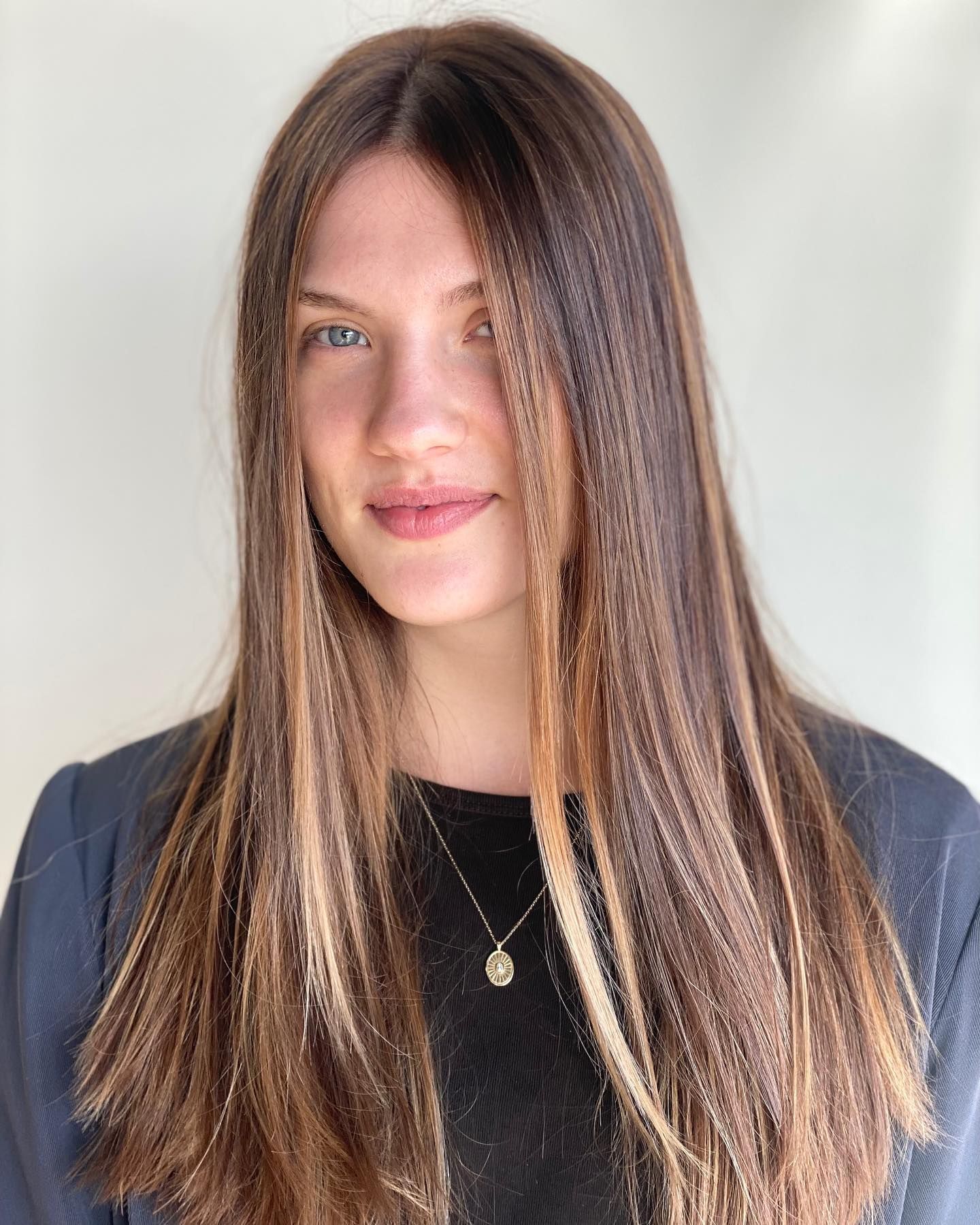 A woman with long brown hair is wearing a black shirt and a necklace.