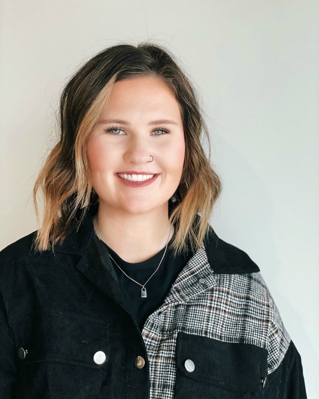 A woman wearing a black jacket and a necklace is smiling for the camera.