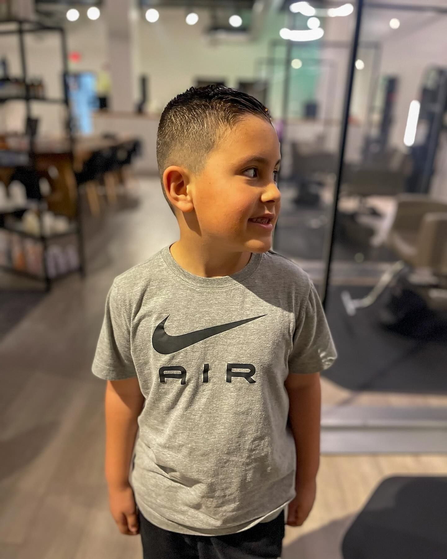 A young boy wearing a grey nike air t-shirt is standing in a gym.