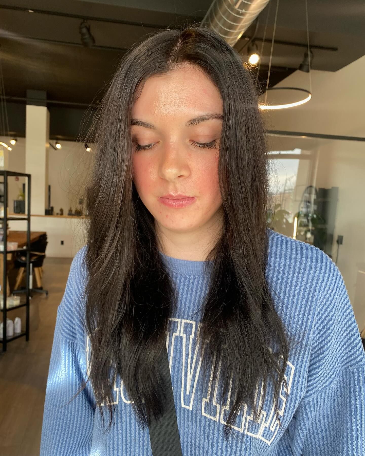 A woman with long black hair is wearing a blue sweater.