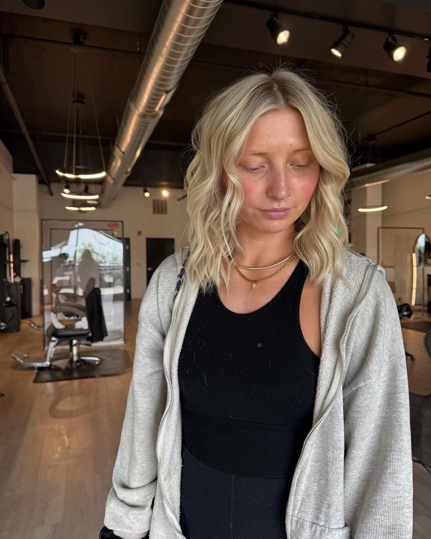 A woman is standing in a salon wearing a gray hoodie and a black tank top.
