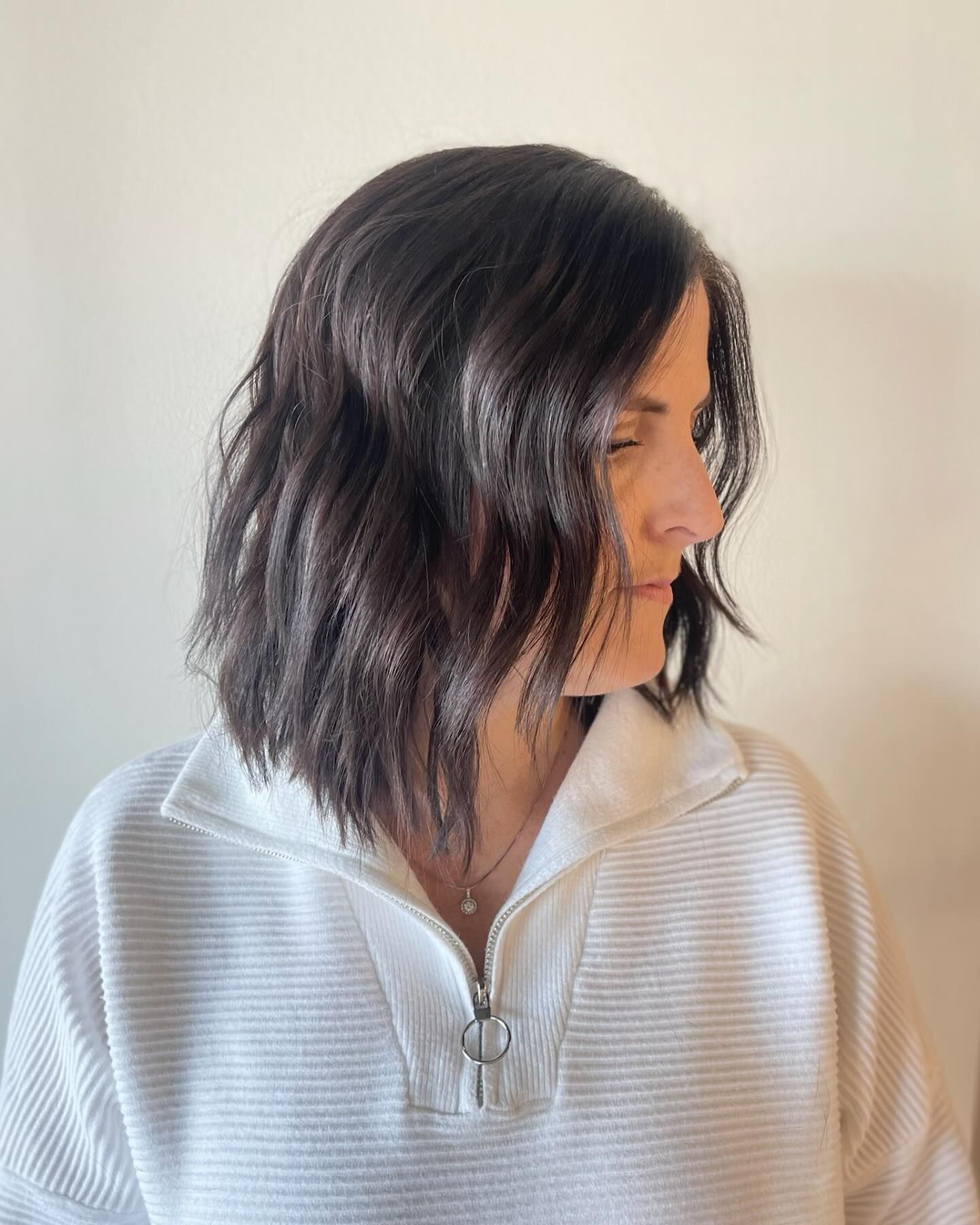 A woman with dark hair is wearing a white sweater with a zipper.