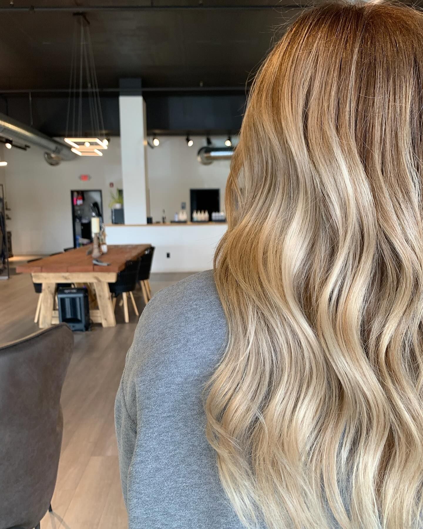 A woman with long blonde hair is standing in a room with a table and chairs.