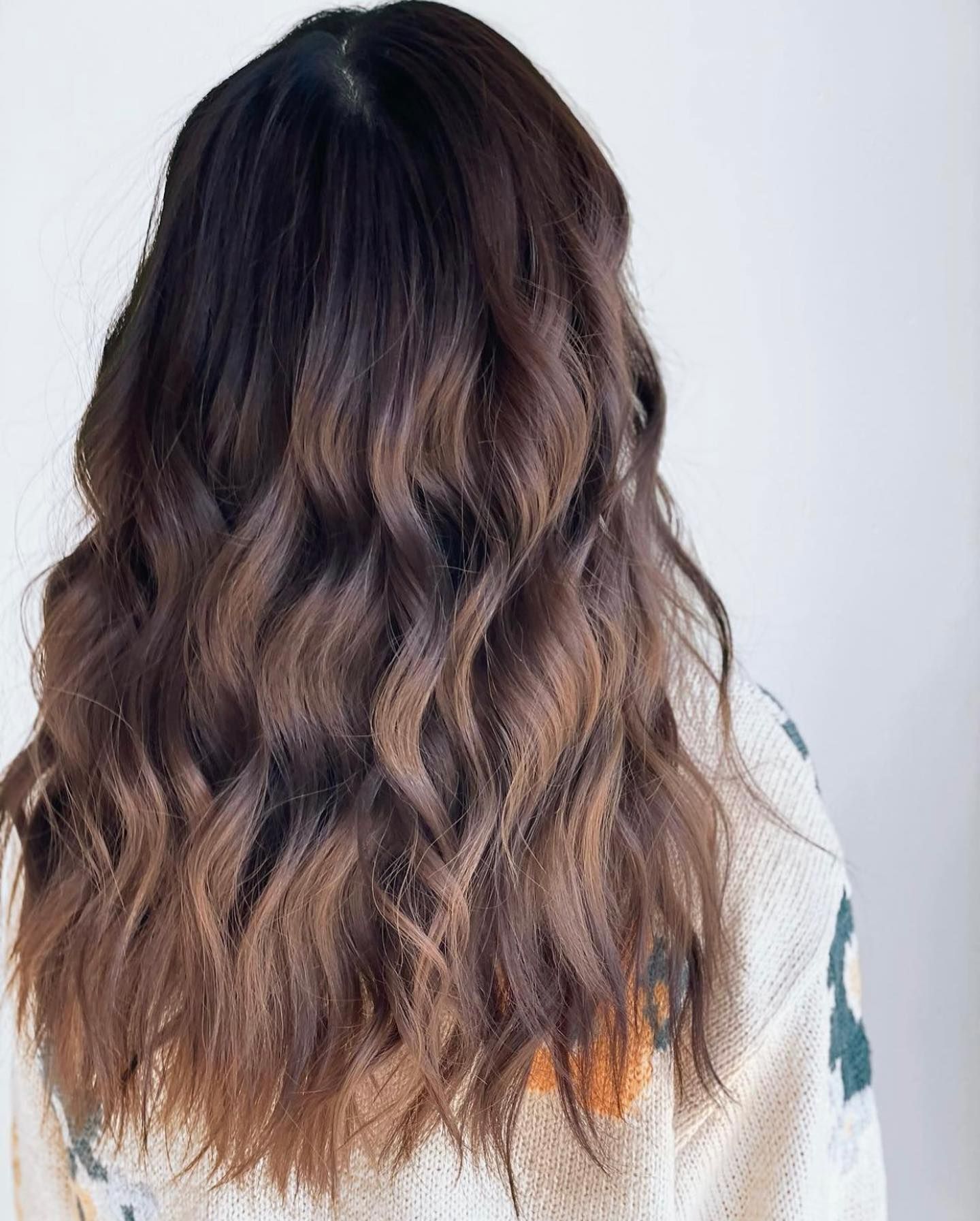 A woman with long wavy brown hair is wearing a white sweater.
