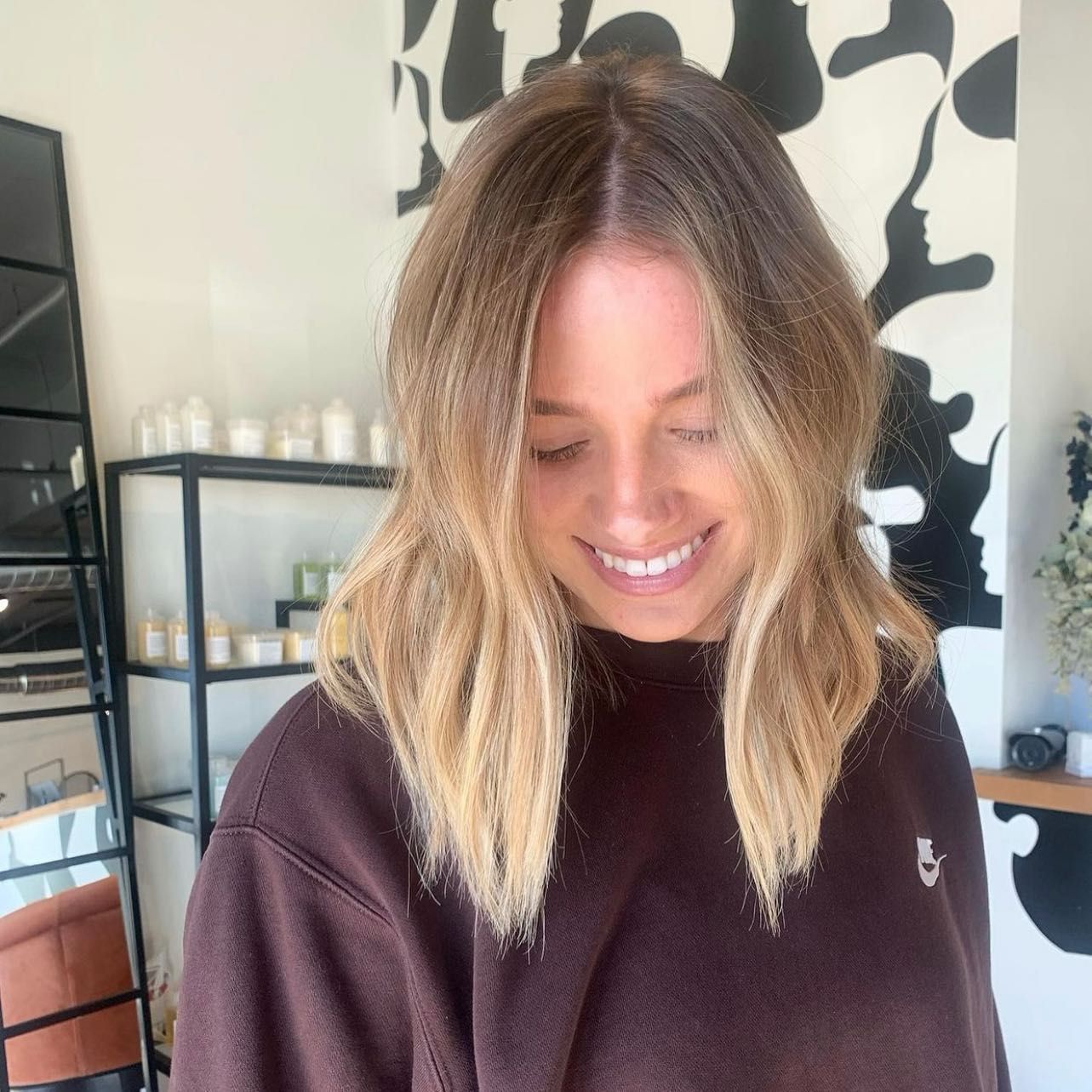 A woman with blonde hair is wearing a brown sweater and smiling.