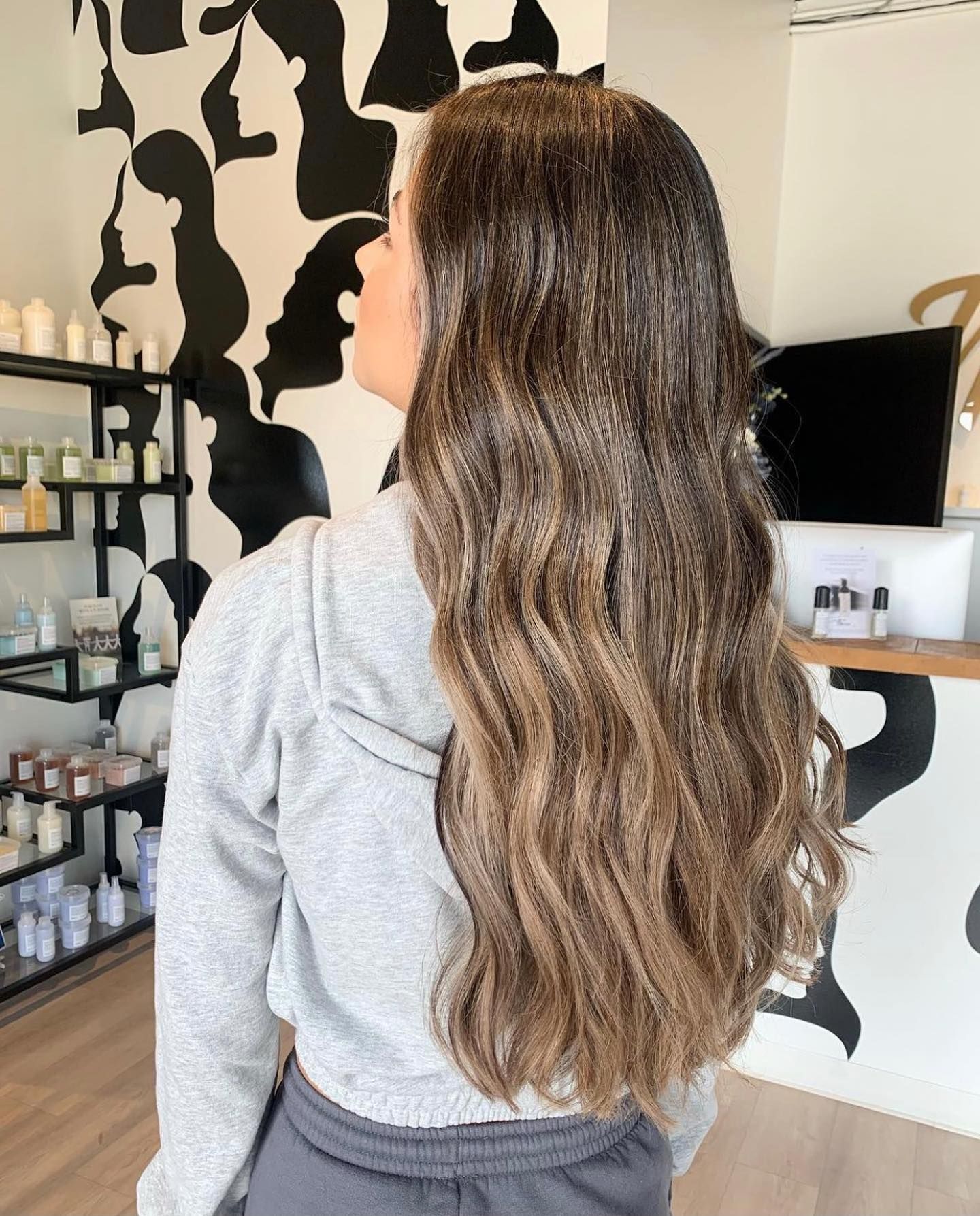 A woman with long brown hair is wearing a grey hoodie and grey sweatpants.