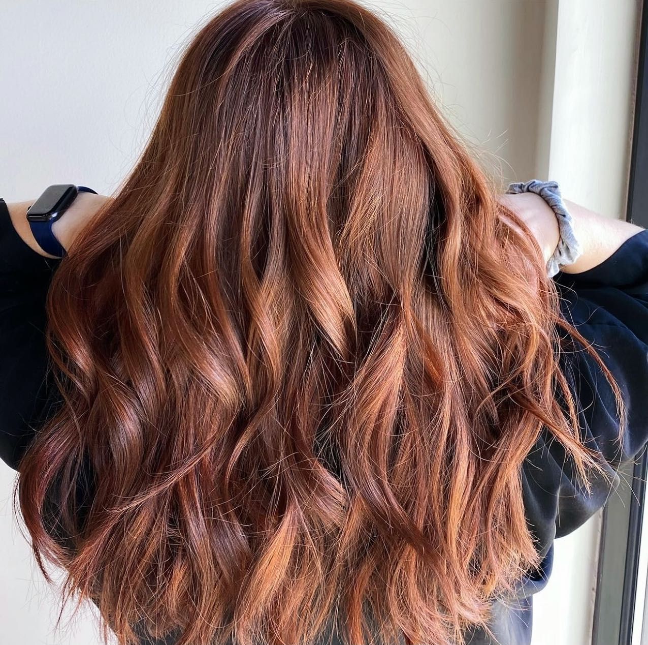 A woman with long brown hair is standing in front of a window.